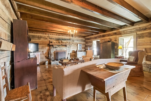 living room featuring beamed ceiling, wood-type flooring, an inviting chandelier, a fireplace, and wood walls