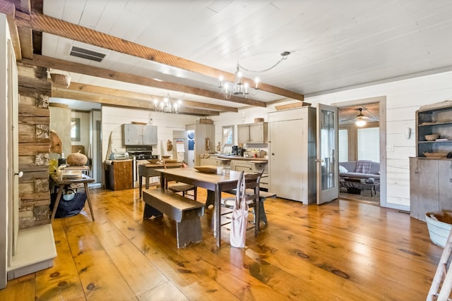 dining room with wood walls, light wood-type flooring, ceiling fan with notable chandelier, wooden ceiling, and beam ceiling