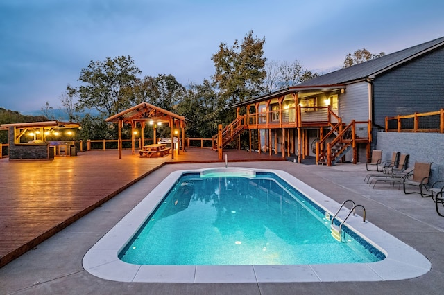 pool at dusk with a patio, a deck, and a gazebo