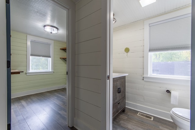 bathroom with toilet, wood walls, vanity, and hardwood / wood-style floors