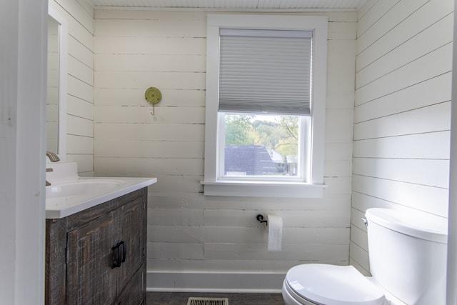 bathroom with vanity, toilet, and wood walls