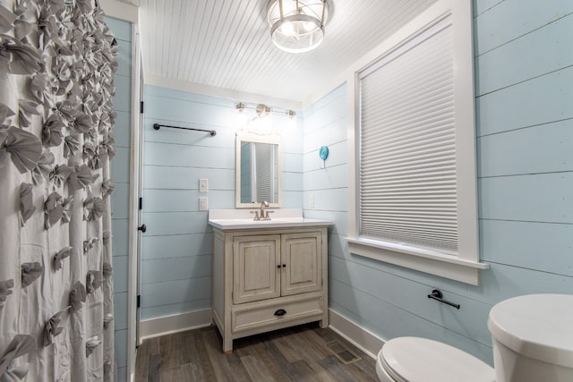 bathroom with wood-type flooring, toilet, a shower with curtain, wooden walls, and vanity