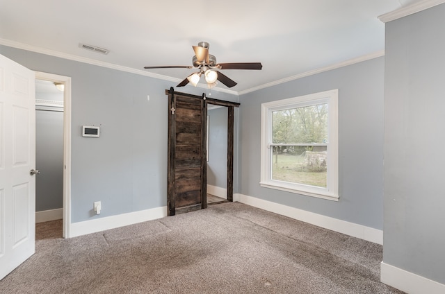 unfurnished bedroom featuring ornamental molding, carpet floors, a barn door, and ceiling fan