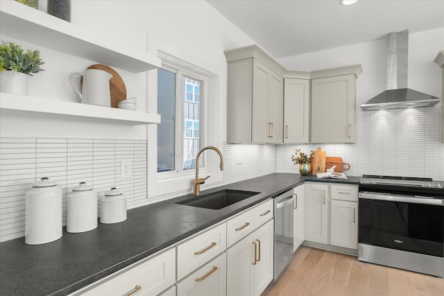 kitchen featuring wall chimney exhaust hood, stainless steel appliances, backsplash, sink, and light wood-type flooring