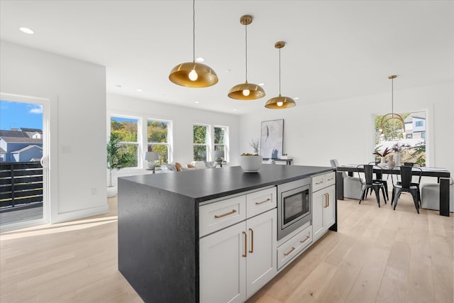 kitchen with stainless steel microwave, hanging light fixtures, a center island, light wood-type flooring, and white cabinetry