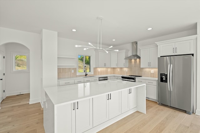 kitchen featuring a wealth of natural light, appliances with stainless steel finishes, wall chimney range hood, and white cabinets