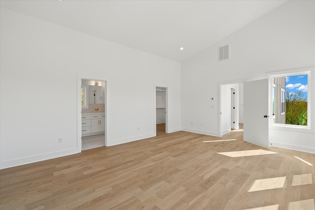 unfurnished bedroom with a spacious closet, connected bathroom, light hardwood / wood-style flooring, and high vaulted ceiling