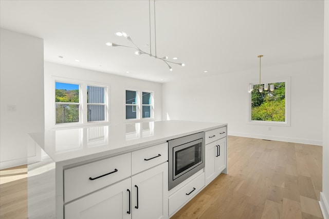 kitchen featuring stainless steel microwave, hanging light fixtures, light wood-type flooring, and a wealth of natural light