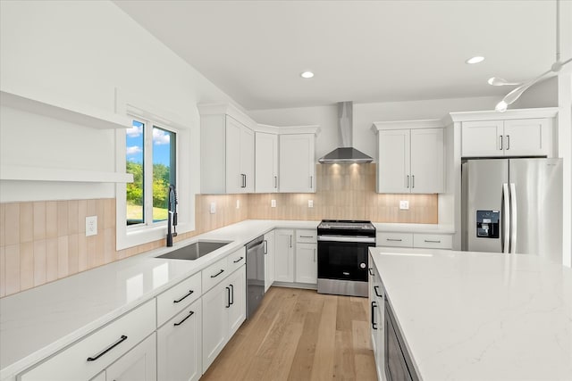 kitchen with white cabinetry, light hardwood / wood-style floors, stainless steel appliances, and wall chimney range hood