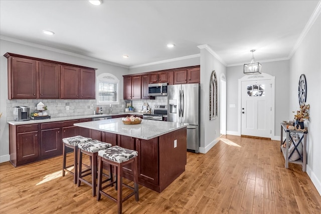 kitchen featuring appliances with stainless steel finishes, a center island, light hardwood / wood-style floors, crown molding, and a breakfast bar area