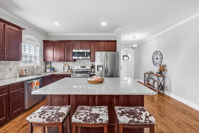 kitchen with light hardwood / wood-style floors, decorative light fixtures, stainless steel appliances, and a kitchen island