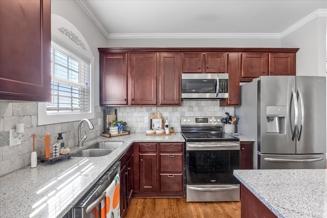 kitchen featuring appliances with stainless steel finishes, light stone countertops, ornamental molding, light hardwood / wood-style floors, and sink