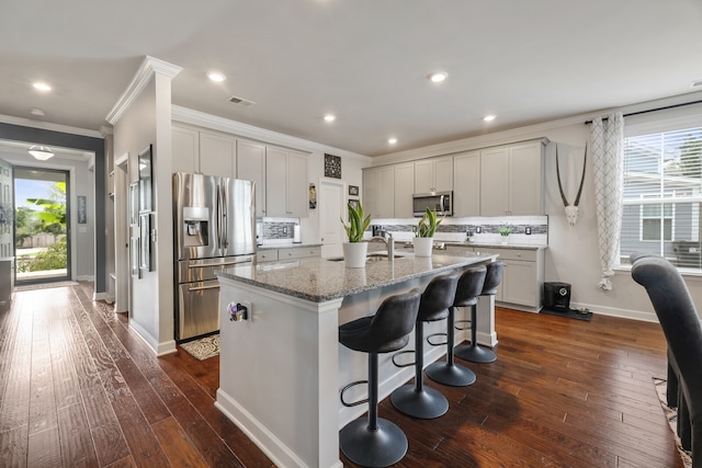 kitchen featuring dark hardwood / wood-style flooring, stainless steel appliances, light stone counters, a breakfast bar area, and a kitchen island with sink