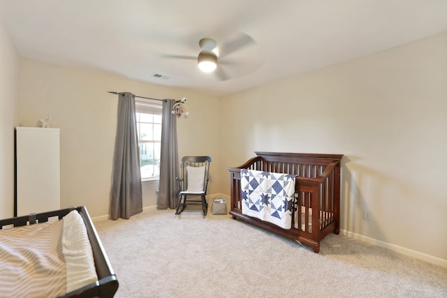 bedroom featuring light carpet, a crib, and ceiling fan