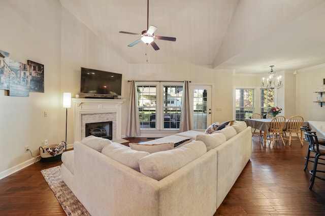 living room with high vaulted ceiling, dark wood-type flooring, ceiling fan with notable chandelier, a stone fireplace, and crown molding