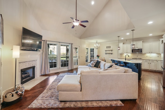 living room featuring sink, ceiling fan with notable chandelier, a stone fireplace, dark hardwood / wood-style flooring, and high vaulted ceiling