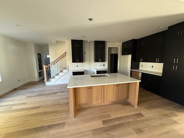 kitchen with light stone countertops, sink, light hardwood / wood-style floors, and an island with sink