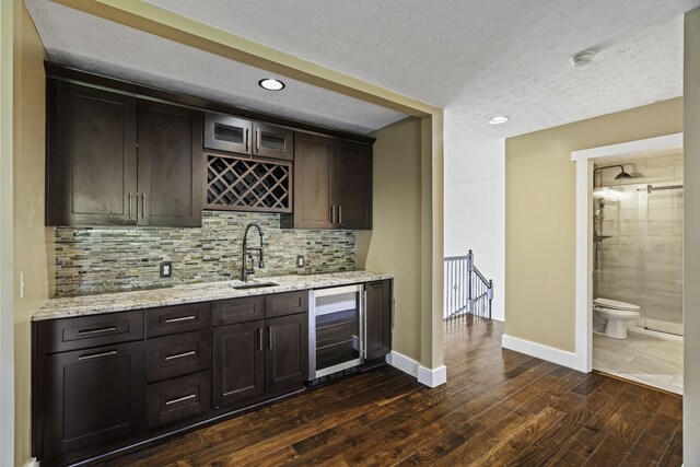 bar with wine cooler, sink, dark brown cabinets, and dark hardwood / wood-style flooring