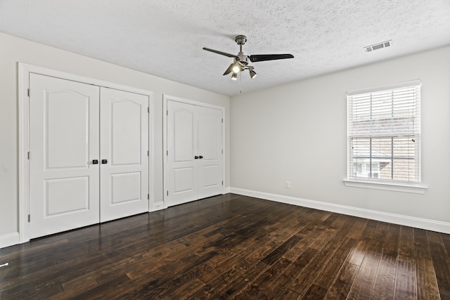 unfurnished bedroom with dark hardwood / wood-style floors, multiple closets, a textured ceiling, and ceiling fan