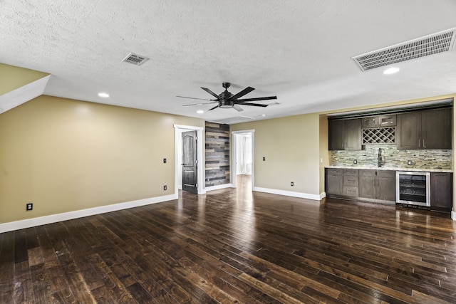 unfurnished living room featuring indoor wet bar, wine cooler, ceiling fan, a textured ceiling, and dark hardwood / wood-style floors