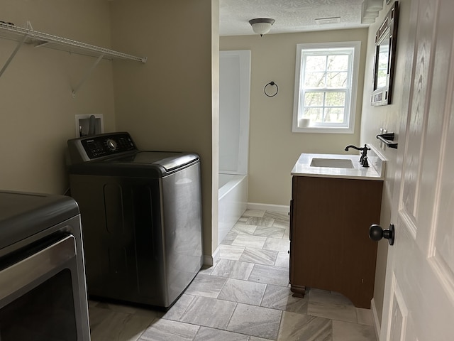 clothes washing area with independent washer and dryer, a textured ceiling, and sink