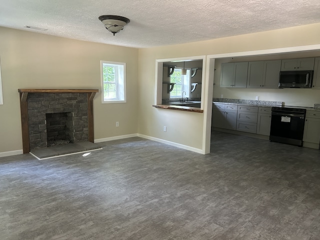 unfurnished living room with dark wood-type flooring, a stone fireplace, a textured ceiling, and sink