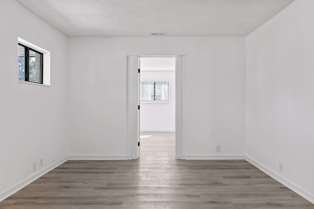 spare room featuring a textured ceiling, wood-type flooring, and a healthy amount of sunlight