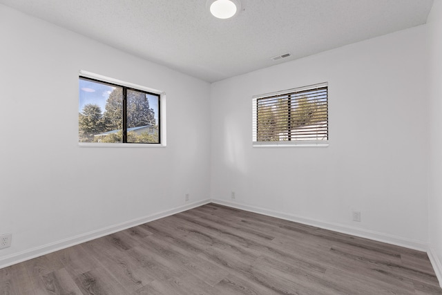 empty room with a textured ceiling, hardwood / wood-style flooring, and a wealth of natural light