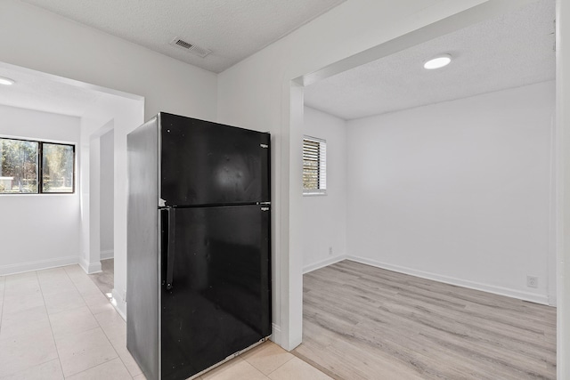 kitchen with black refrigerator, a textured ceiling, and light wood-type flooring