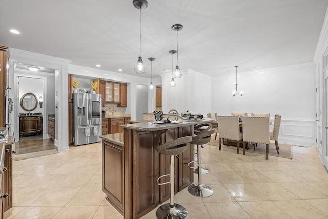 kitchen with a center island, hanging light fixtures, crown molding, a breakfast bar, and stainless steel refrigerator with ice dispenser