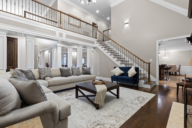 living room with a high ceiling, ornate columns, hardwood / wood-style flooring, crown molding, and a notable chandelier