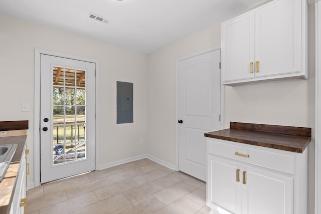 kitchen featuring white cabinets, butcher block counters, light tile patterned floors, and electric panel