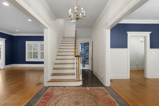 stairs with wood-type flooring, ornamental molding, and an inviting chandelier