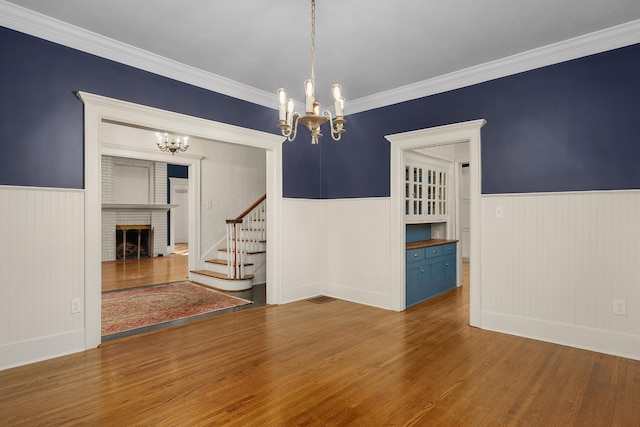 empty room featuring an inviting chandelier, crown molding, hardwood / wood-style flooring, and a brick fireplace