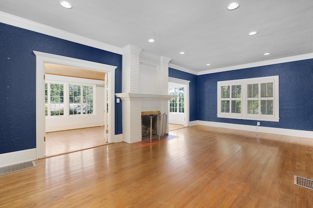 unfurnished living room with light hardwood / wood-style floors, crown molding, a wealth of natural light, and a brick fireplace