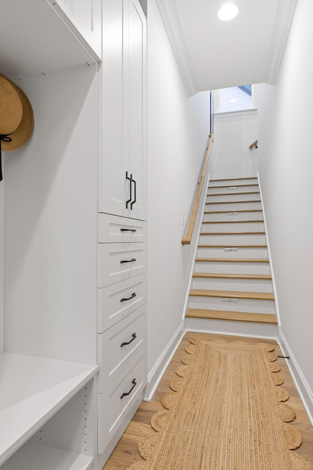 staircase with wood-type flooring and ornamental molding