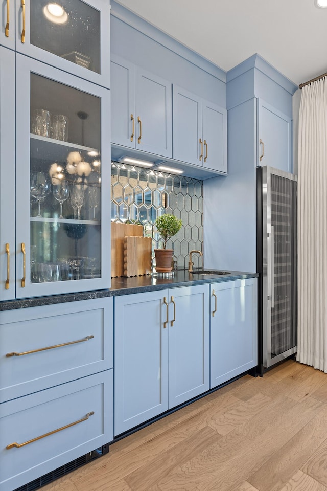 bar featuring sink, light hardwood / wood-style flooring, stainless steel fridge, decorative backsplash, and white cabinets