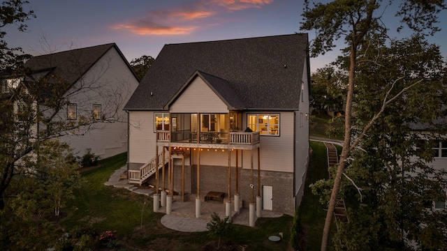 back house at dusk featuring a balcony and a patio