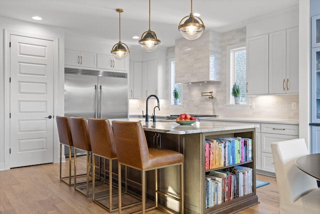 kitchen with white cabinetry, sink, light stone countertops, a kitchen breakfast bar, and an island with sink