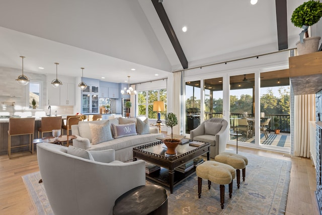 living room with beam ceiling, sink, high vaulted ceiling, ceiling fan with notable chandelier, and light wood-type flooring