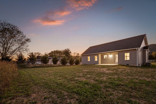 back house at dusk featuring central AC and a lawn