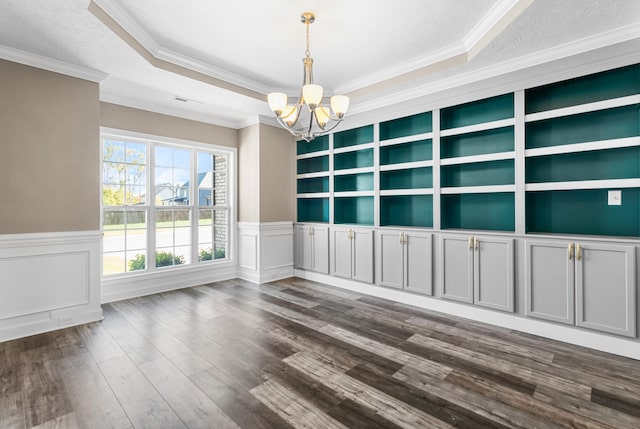 empty room featuring dark wood-type flooring, a tray ceiling, built in features, and ornamental molding