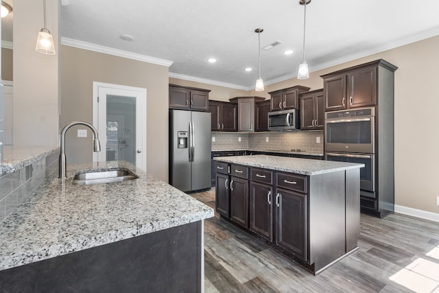 kitchen featuring hanging light fixtures, appliances with stainless steel finishes, wood-type flooring, ornamental molding, and sink