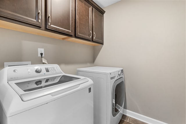 clothes washing area featuring cabinets, dark tile patterned floors, and washing machine and dryer