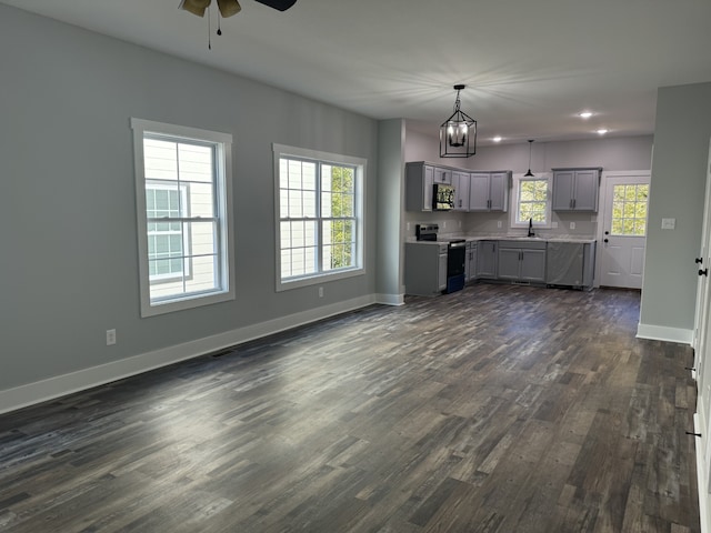 unfurnished living room with sink, ceiling fan with notable chandelier, and dark hardwood / wood-style flooring