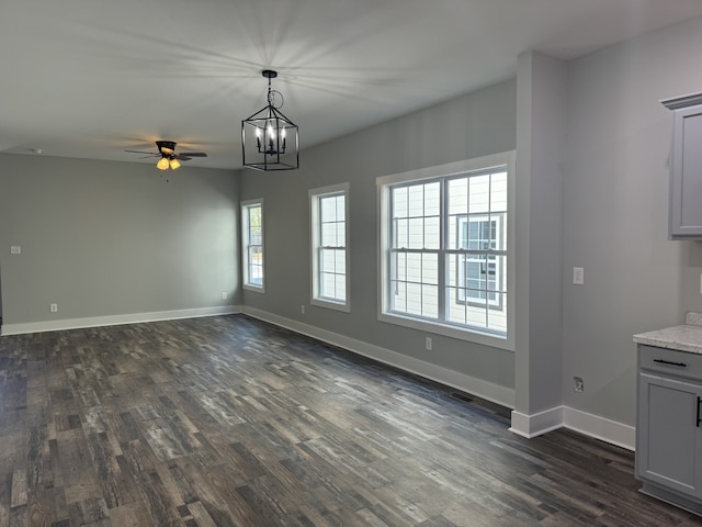 unfurnished dining area featuring ceiling fan with notable chandelier and dark hardwood / wood-style flooring