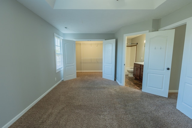 unfurnished bedroom with a spacious closet, a closet, ensuite bath, and carpet flooring