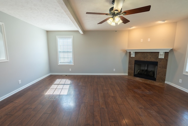 unfurnished living room featuring a fireplace, beamed ceiling, dark hardwood / wood-style flooring, a textured ceiling, and ceiling fan