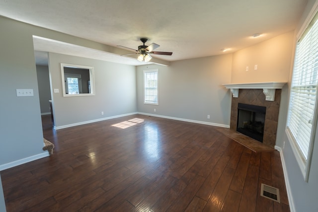 unfurnished living room featuring dark wood-type flooring, a tiled fireplace, and ceiling fan