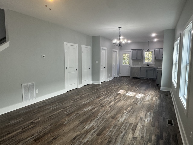 unfurnished living room featuring an inviting chandelier, sink, and dark wood-type flooring